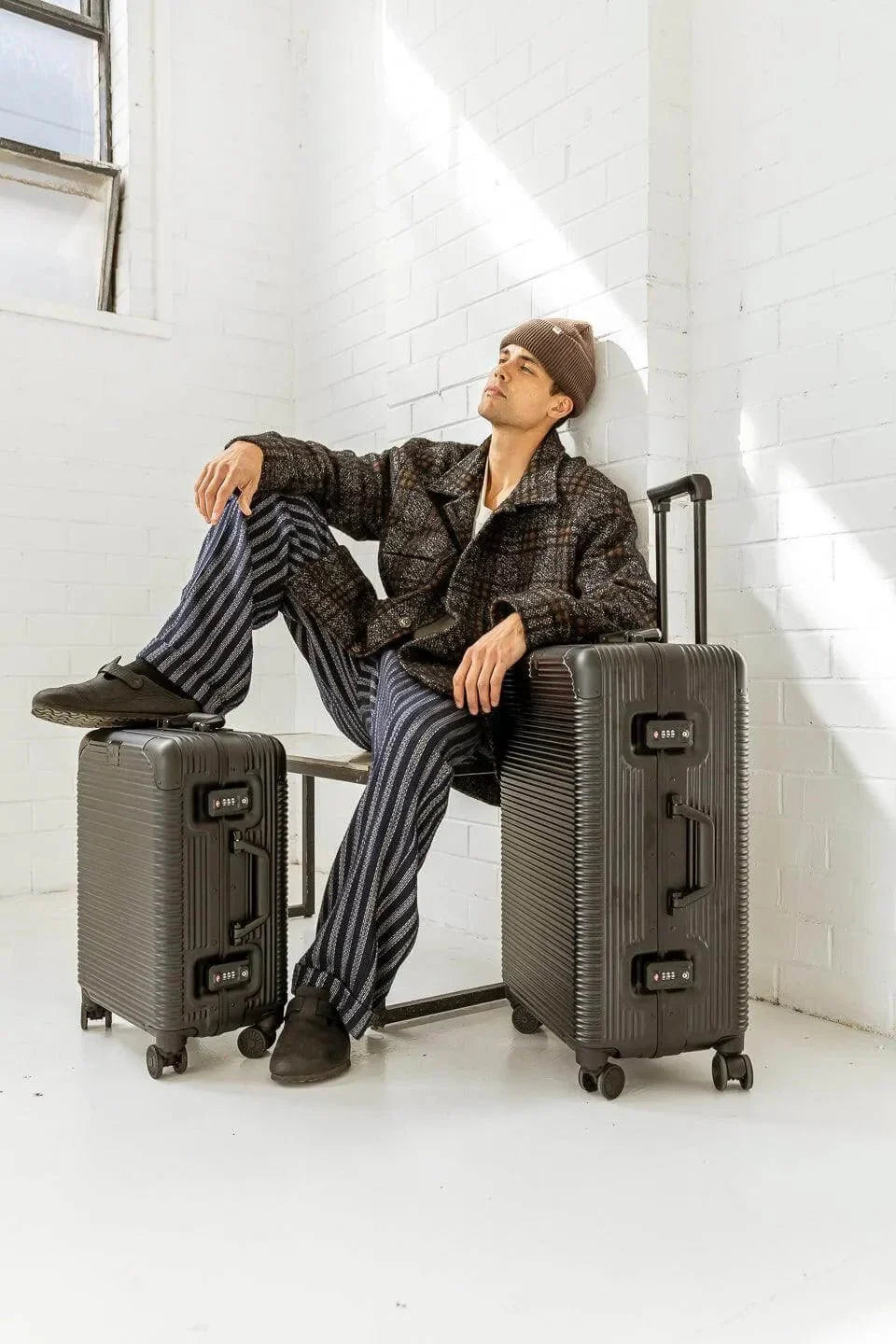 A stylish individual seated on a chair with two modern suitcases, showcasing urban travel fashion.