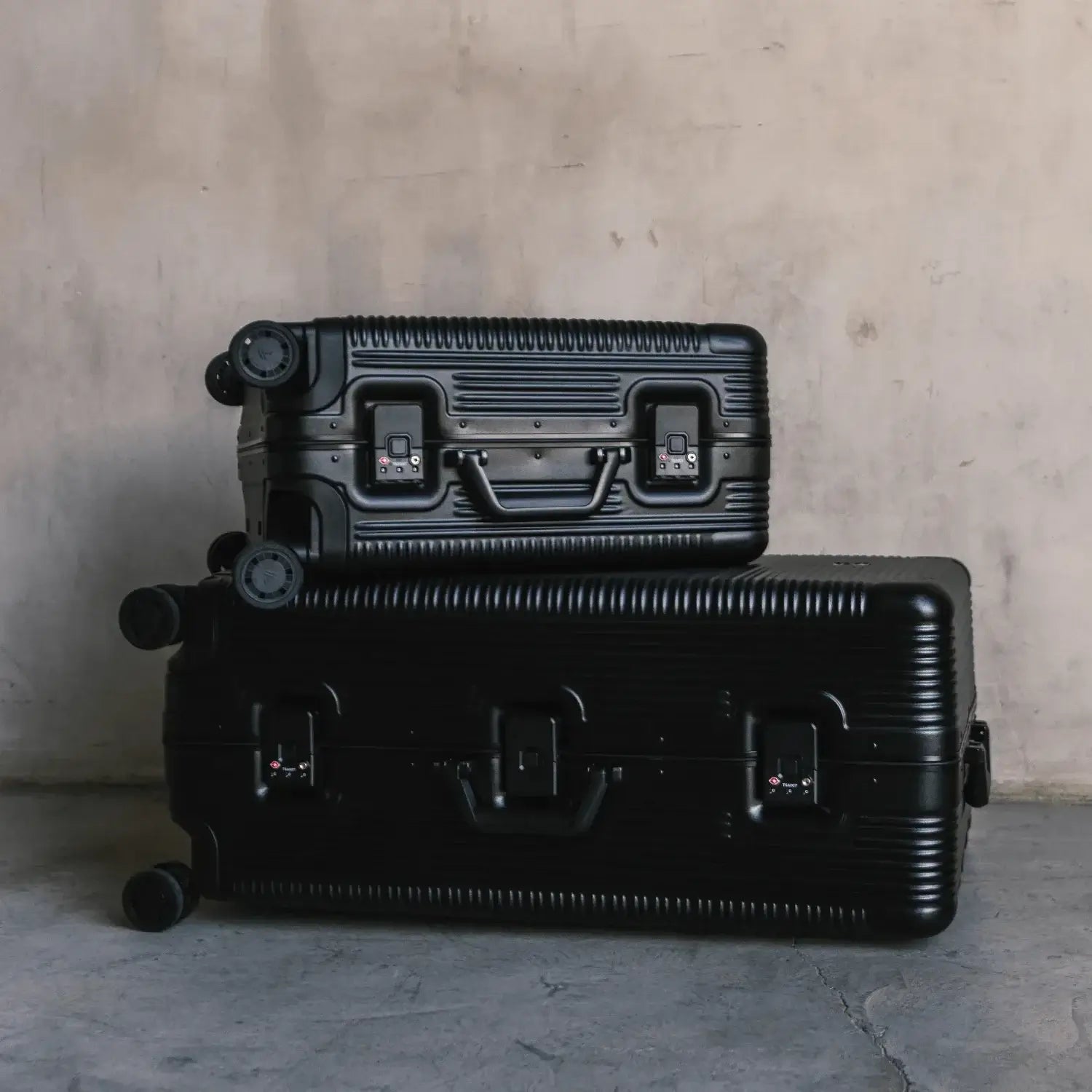 Stylish black luggage stacked against a textured wall, ideal for travel enthusiasts and adventure seekers.