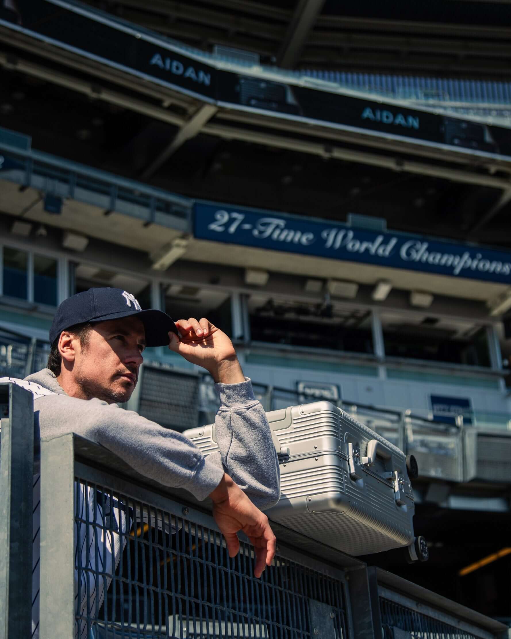 Man wearing a New York Yankees cap and Aidan sweatshirts at Yankee Stadium, showcasing sports fashion.